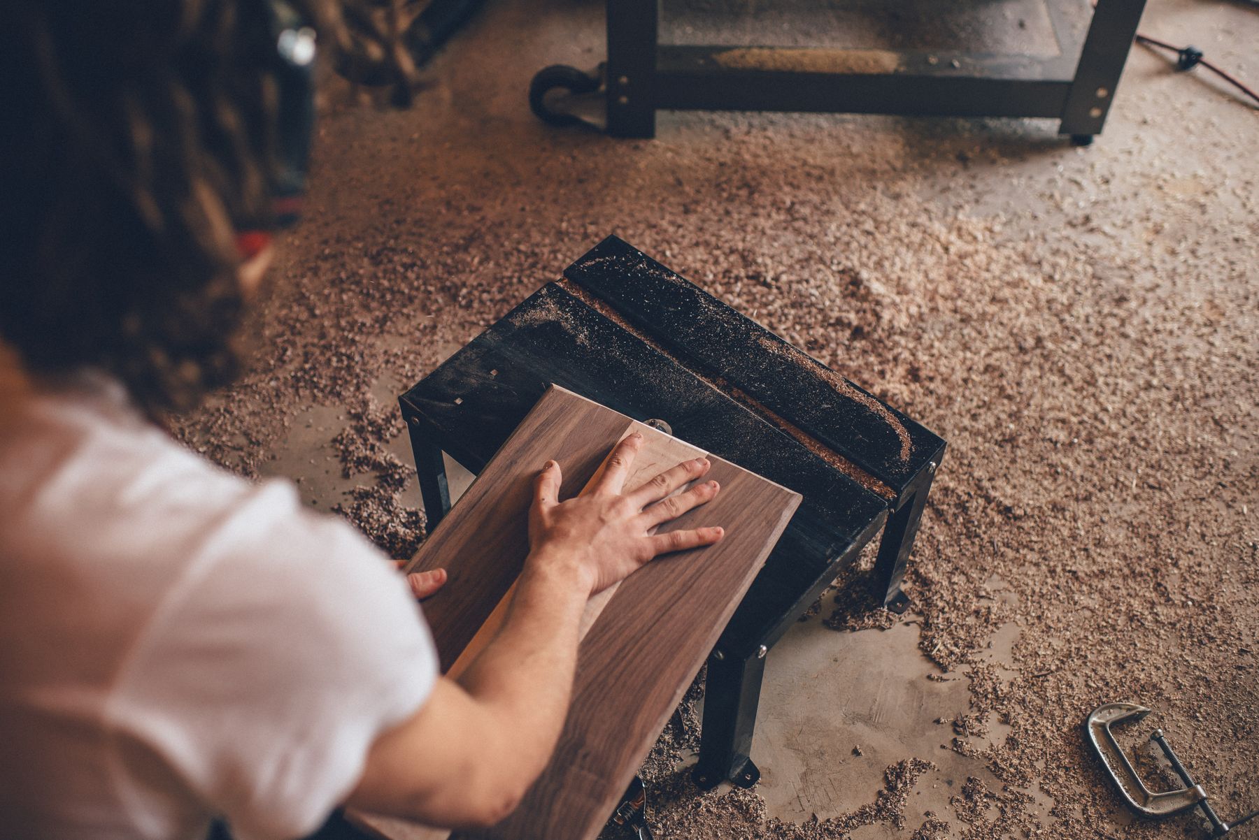Hands working a board on a workbench covered in sawdust
