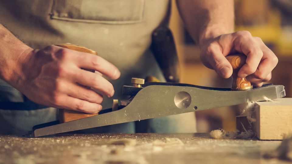 Hands pushing a hand plane along a board with shavings curling off