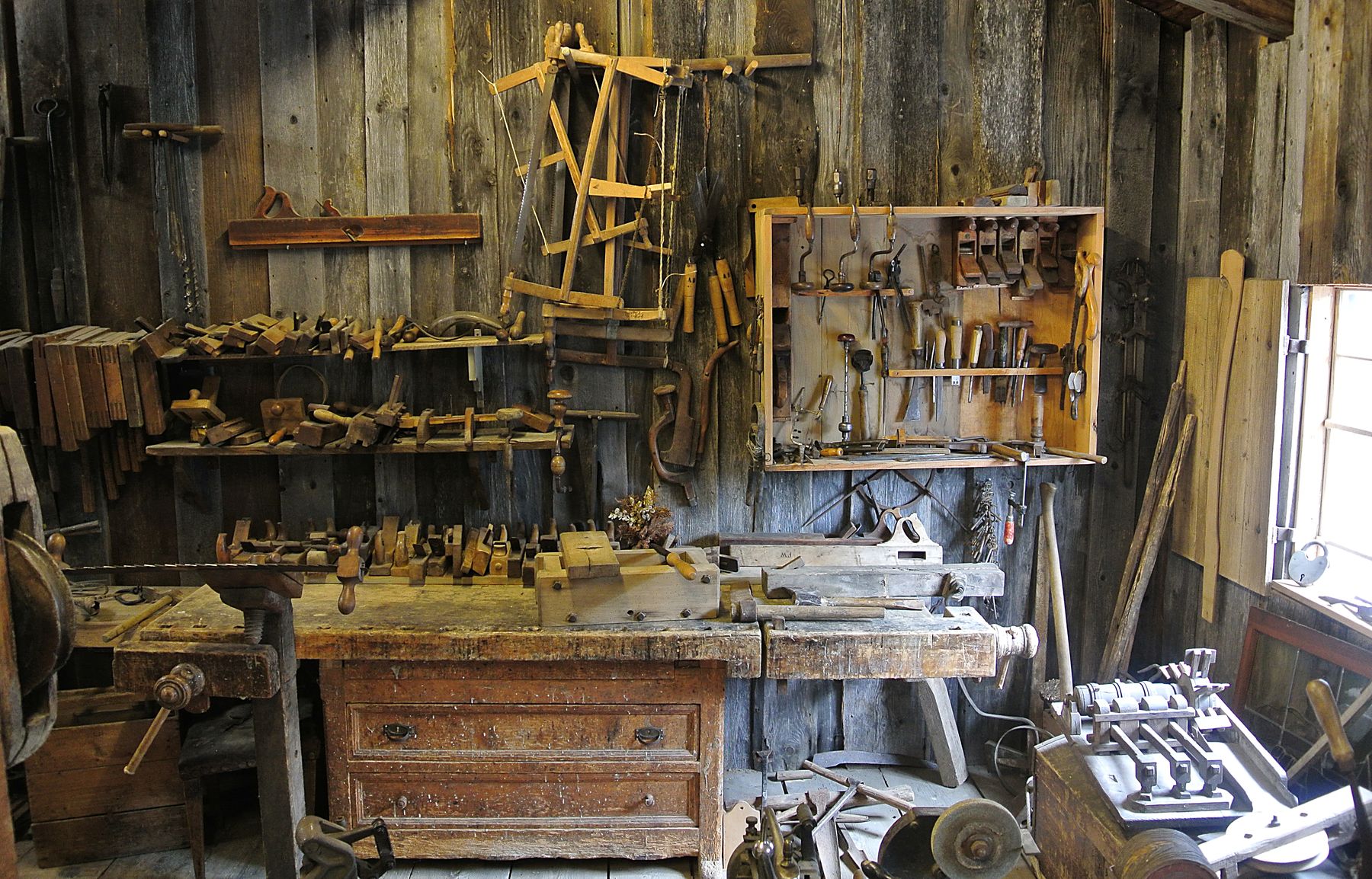 Interior of a small woodworking shop with hand tools on the wall and chairs in progress