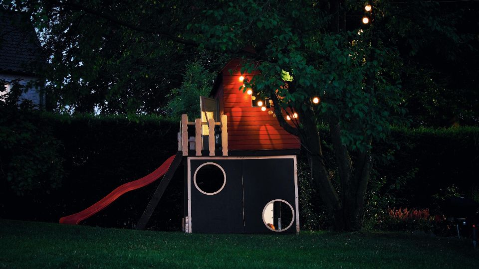 Small wooden playhouse lit up in a backyard at dusk